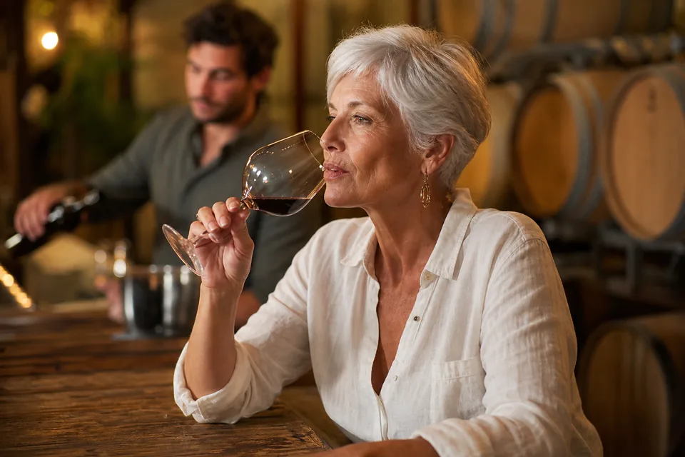 Woman in her late fifties tasting wine at a vineyard bar in the evening, illustrative photo, not a member